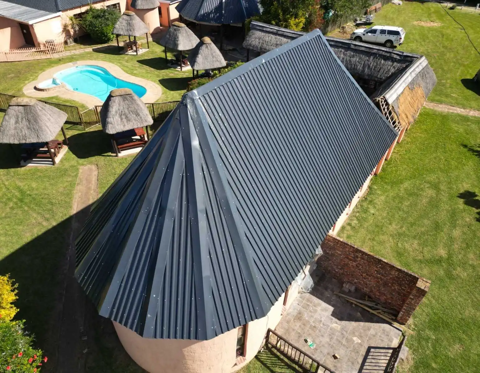Converted roof on a round building with thatched gazebos and a pool nearby